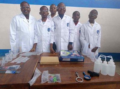 Six students in lab coats and goggles behind a bench of laboratory glassware