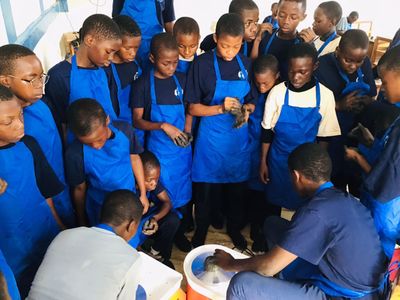 Students in blue aprons gathered around a potter's wheel demonstration