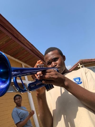 A student playing a blue trumpet against a clear sky