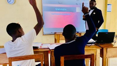 A teacher leading a French grammar lesson while two students raise their hands to answer