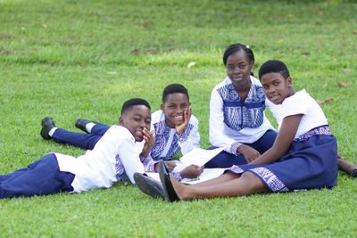 Four students in Ndop uniform sitting together on the grass, sharing a printed sheet of work