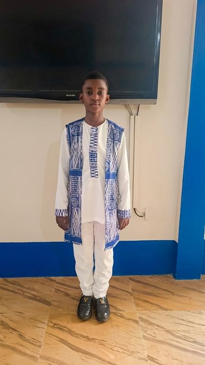 A student in ceremonial dress: a white tunic and trousers worn under a long waistcoat in blue Ndop cloth