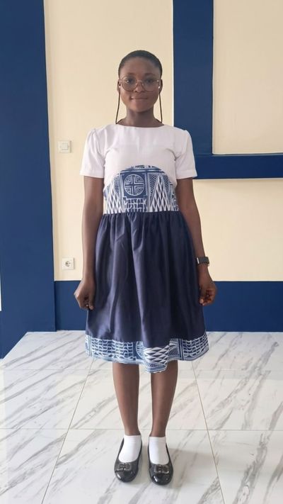 A student in the formal uniform for girls: a white bodice with an Ndop panel at the waist and a navy skirt with an Ndop hem border